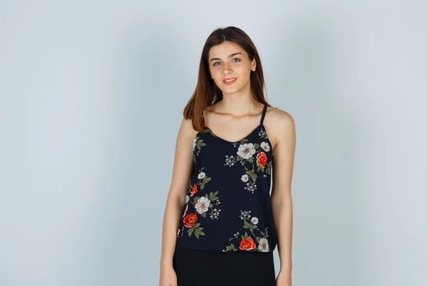 Jeune femme debout portant un débardeur noir à fleurs colorées, posant devant un fond gris clair.Les gîtes du haut bois 2 Le Haut Bois, 25650 Ville-du-Pont, France